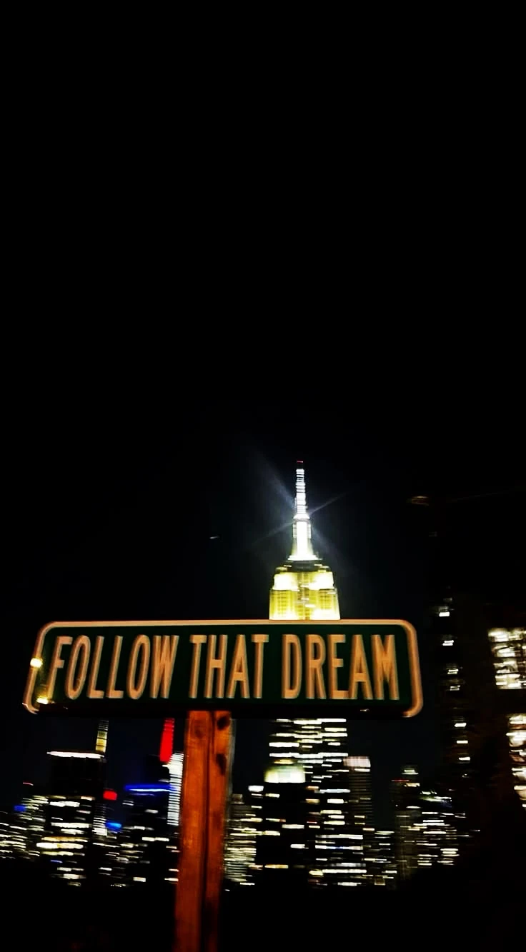 Znak FOLLOW THAT DREAM na tle nocnych wieżowców